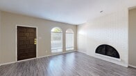 This single-story, one-bedroom, one-bathroom unit offers a thoughtfully arranged layout across a compact yet functional floor plan. The living room serves as the centerpiece of the unit, immediately capturing attention with its pair of arched windows that flood the space with natural light. A full-wall white brick fireplace with an arched hearth anchors one side of the room, adding architectural character and warmth. Wood-look flooring in a cool gray tone extends throughout, providing a cohesive and modern aesthetic.

The kitchen features a peninsula-style counter that separates it from the main living area, offering both workspace and an open connection to the rest of the unit. White cabinetry with understated hardware provides ample storage, and the layout includes a range and refrigerator.

The generously sized primary bedroom accommodates a comfortable living arrangement and includes a built-in closet. Its neutral walls and wood-look flooring maintain the consistent design language of the unit.

The bathroom stands out with dual marble-patterned vanity countertops flanking a central wet area, which includes a tiled tub-shower combination. Large mirrors above each vanity enhance the sense of space. Two hallways connect the rooms, contributing to an efficient and logical flow throughout.