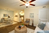 Located at 624 Suhtai Ct in Virginia Beach, VA, this single-floor residence offers a well-designed layout with a cohesive coastal aesthetic throughout. The living room is bright and welcoming, featuring hardwood-style flooring, a ceiling fan, and a large window with blinds that allows natural light to fill the space. The relaxed furnishing arrangement, including a woven ottoman and rattan accent chair, reinforces the coastal tone.

The dining area connects seamlessly to the kitchen through a pass-through opening, with soft blue accent walls and track lighting adding character. The kitchen is efficiently designed with white shaker-style cabinetry, stainless steel appliances including a range, microwave, and dishwasher, and a neutral countertop with an integrated sink.

The primary bedroom features hardwood-style flooring, a generous window, and a walk-in closet, providing comfortable storage. A second bedroom serves well as a home office or guest room, also equipped with a closet and natural light from a window with decorative curtains. The bathroom includes a full tub-shower combination with clean white tile surround. A dedicated laundry area houses an in-unit washer and water heater, adding everyday convenience to this thoughtfully appointed Virginia Beach home.