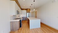 This contemporary two-story home in Phoenix, AZ offers a thoughtfully designed layout spread across two floors. The ground level houses an attached garage finished with durable epoxy-coated flooring, a glass-panel door, and direct interior access — a clean, functional space equipped with a water heater and electrical panel. A staircase leads to the main living level above, where light hardwood flooring flows throughout.

The designer kitchen is a standout feature, showcasing a striking marble-look quartz island, two-tone cabinetry combining crisp white uppers with warm wood-grain lowers, stainless steel appliances including a gas range, and elegant glass pendant lighting. The open layout and recessed lighting contribute to a bright, welcoming atmosphere.

Both bedrooms are generously proportioned, each featuring light hardwood floors, black-framed sliding windows with natural views, and ceiling fans. The spacious primary bedroom includes its own closet and an en suite bathroom outfitted with a wood-tone floating vanity, white quartz countertop, brushed gold fixtures, stone tile flooring, and a glass-enclosed walk-in shower. The secondary bathroom features similar warm finishes with a tub-shower combination and tasteful tile surround. Two closets offer ample storage throughout the home.