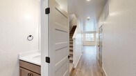 Located in Coeur d'Alene, Idaho, this well-designed two-story home offers three bedrooms and three bathrooms across two thoughtfully laid-out floors. The main level features an open-concept kitchen and living area finished with light hardwood-style flooring throughout. The kitchen is appointed with warm-toned cabinetry, stainless steel appliances including a refrigerator and microwave, a central island with pendant lighting, and clean white countertops. The living room benefits from multiple windows and a ceiling fan, creating a bright and airy atmosphere with access to an exterior door. Hallways on both levels connect the spaces efficiently, with shaker-style interior doors featuring matte black hardware adding a contemporary touch. The upper floor houses the three bedrooms, including a generously sized primary bedroom with its own walk-in closet equipped with wire shelving systems for organized storage. Each bathroom is finished with wood-toned vanities, white countertops, and hardwood-style flooring, with at least one bathroom offering a walk-in shower and a window for natural light. A dedicated laundry room with side-by-side washer and dryer and upper cabinetry adds everyday convenience. The home presents a clean, modern aesthetic throughout.