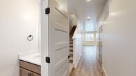 Located in Coeur d'Alene, Idaho, this well-designed two-story home offers three bedrooms and three bathrooms across two thoughtfully laid-out floors. The main level features an open-concept kitchen and living area finished with light hardwood-style flooring throughout. The kitchen is appointed with warm-toned cabinetry, stainless steel appliances including a refrigerator and microwave, a central island with pendant lighting, and clean white countertops. The living room benefits from multiple windows and a ceiling fan, creating a bright and airy atmosphere with access to an exterior door. Hallways on both levels connect the spaces efficiently, with shaker-style interior doors featuring matte black hardware adding a contemporary touch. The upper floor houses the three bedrooms, including a generously sized primary bedroom with its own walk-in closet equipped with wire shelving systems for organized storage. Each bathroom is finished with wood-toned vanities, white countertops, and hardwood-style flooring, with at least one bathroom offering a walk-in shower and a window for natural light. A dedicated laundry room with side-by-side washer and dryer and upper cabinetry adds everyday convenience. The home presents a clean, modern aesthetic throughout.