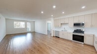 This thoughtfully designed single-floor residence features three bedrooms, two bathrooms, and a generous open-concept living area that seamlessly connects the kitchen, dining, and living spaces. Warm wood-look flooring runs consistently throughout, lending a cohesive and inviting feel to the entire home.

The kitchen is a standout feature, showcasing light-toned flat-panel cabinetry with ample upper and lower storage, white quartz countertops, a clean tile backsplash, and a full suite of stainless steel appliances including a gas range, microwave, dishwasher, and French door refrigerator. Recessed lighting illuminates the space efficiently. The open living room benefits from natural light provided by a large window and a glass-paneled entry door.

The spacious primary bedroom offers generous proportions and is served by a dedicated walk-in closet with dual hanging rods and built-in shelving. The additional bedrooms each feature wood-look flooring and windows fitted with vertical blinds, allowing for adjustable natural light. Both bathrooms are finished with light wood vanity cabinetry, white countertops, and clean, modern fixtures. A hallway connects the private areas of the home, contributing to a practical and well-organized floor plan throughout.