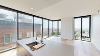 This contemporary 2-bedroom, 2-bathroom residence is designed with a clean, modern aesthetic throughout. Light hardwood flooring runs continuously across the entire single-floor layout, lending warmth and cohesion to the space. The open-concept kitchen and living area serves as the heart of the home, anchored by dramatic floor-to-ceiling windows on two walls that frame sweeping panoramic city views and flood the space with natural light. The kitchen is outfitted with rich walnut cabinetry, stainless steel appliances, a mosaic tile backsplash, and a generous island with a quartz countertop and integrated sink — ideal for both cooking and entertaining. The living area benefits from the same expansive corner glazing, creating a bright and airy atmosphere with unobstructed urban vistas. Both bedrooms continue the floor-to-ceiling window motif, offering abundant natural light and impressive elevated views of the cityscape. The primary bedroom is comfortably sized, while the second bedroom provides a clean, versatile space. A light-filled hallway with recessed lighting connects the rooms. The bathrooms feature large-format tile and frameless glass shower enclosures, conveying a refined, spa-like quality. Overall, the residence presents a cohesive, upscale modern design with standout views at every turn.