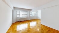 Unit 716 at 825 New Hampshire Ave NW is a one-bedroom, one-bathroom residence located in Washington, DC's Foggy Bottom neighborhood. The unit spans a comfortable single floor, offering a well-organized layout that includes a living room, bedroom, kitchen, bathroom, and hallway.

The living room is a standout feature, characterized by gleaming parquet hardwood floors in a warm honey tone and two large windows fitted with horizontal blinds that admit generous natural light and provide views of the surrounding cityscape. A baseboard heating unit runs along the exterior wall beneath the windows.

The spacious primary bedroom continues the parquet flooring and features a window with an exterior view, a closet, and clean white walls, creating a bright and functional space.

The kitchen is outfitted with white cabinetry, granite-look countertops, a stainless steel undermount sink, and a white gas range. Cork-style flooring and ample cabinet storage complete the practical cooking space.

The bathroom is finished with white ceramic wall tiles, a combined tub and shower with a chrome showerhead, a white vanity with under-sink storage, and a mirrored medicine cabinet above.

Throughout the unit, the consistent use of light, neutral tones and natural wood flooring creates a cohesive and functional living environment.