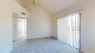This single-floor residence offers a thoughtfully arranged layout that maximizes comfort and functionality throughout. The living area is a standout, boasting dramatic vaulted ceilings that lend a sense of openness and volume to the space. A large sliding glass door fitted with vertical blinds floods the room with natural light while providing outdoor access and views. The flooring transitions seamlessly from plush carpet in the living and bedroom areas to wood-look hard flooring in the entry and kitchen zones.

The galley-style kitchen is efficiently designed with light wood cabinetry lining both walls, dark speckled countertops, a double stainless steel sink, and white appliances including a range and refrigerator. The space is practical and well-organized for everyday use.

The bedrooms continue the vaulted ceiling design, each featuring soft carpet, generous natural light from windows dressed with vertical blinds, and built-in closets with shelving and hanging rods for ample storage. One bedroom includes a particularly spacious closet with dedicated shelving tiers.

The bathrooms are finished consistently with dark speckled countertops, wood-toned vanity cabinetry, and wood-look tile flooring. One bathroom features a tub-shower combination with clean white tile surround. The overall palette throughout is neutral and bright, creating a calm, move-in-ready atmosphere.