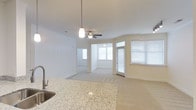 This single-floor residence offers a clean, open-concept design that seamlessly connects the kitchen and living areas into one cohesive, light-filled space. The kitchen is appointed with rich dark cabinetry, granite countertops, a stainless steel refrigerator, and a sink with a modern faucet — providing both style and functionality. A peninsula counter serves as a natural divider between the kitchen and the adjoining living and dining areas, making it ideal for entertaining.

The living space is generously proportioned, featuring plush wall-to-wall carpeting that adds warmth and comfort underfoot. Ceiling fans are installed throughout, contributing to the home's year-round comfort and airy feel. Track lighting complements the pendant light fixtures, ensuring well-distributed illumination across the open floor plan.

Multiple windows dressed with horizontal blinds allow natural light to pour in from several angles, creating a bright and welcoming ambiance throughout the day. The neutral white and beige color palette enhances the sense of openness, while the smooth, clean walls and consistent finishes lend the space a modern, well-maintained aesthetic. The layout flows intuitively, offering a comfortable and functional living environment.