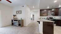This single-floor residence offers a well-organized layout that maximizes functionality across its living areas. The kitchen serves as a central highlight, featuring rich dark-stained cabinetry, granite-look countertops, a breakfast bar peninsula, and stainless steel appliances including a refrigerator, range, and microwave. Light wood-style flooring runs through the kitchen and dining area, where a chandelier adds a refined touch overhead.

The open flow from the kitchen leads into a carpeted living area, framed by clean white walls and recessed lighting. A hallway connects the main living space to the private areas of the home, including bedrooms finished with plush carpet, ample natural light from well-placed windows, and sliding-door closets offering generous storage.

The bathroom presents a clean, minimal aesthetic with a full tub-shower combination, white tile surround, and wood-style tile flooring. A dedicated laundry area accommodates a full-sized side-by-side washer and dryer with overhead shelving for additional storage. Throughout the residence, crisp white walls, consistent flooring materials, and practical storage solutions—including walk-in and reach-in closets—contribute to a cohesive, move-in-ready atmosphere.