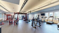 Located at 1 Haddon Blvd in Mount Laurel, NJ, this fitness center offers a generously sized, single-floor exercise space designed to accommodate a wide range of workout styles. The layout is thoughtfully organized, with distinct zones dedicated to cardio, strength training, and functional fitness.

The cardio area is lined with large windows that flood the space with natural light and provide pleasant outdoor views of the surrounding community, creating an energizing environment for treadmill and elliptical workouts. A dedicated strength zone features multi-tiered dumbbell racks stocked with a full range of free weights, adjustable benches, and Rogue-branded equipment, ideal for resistance training.

A prominent functional training section sits at the heart of the space, anchored by a large multi-station cable and power rack system in bold red, accommodating simultaneous users across various exercises. A heavy punching bag adds a combat fitness element to the mix.

The interior design features durable rubber flooring throughout, recessed and tray ceiling lighting, crisp white walls accented by a bold blue feature wall, and motivational quotes inscribed along the upper walls — including phrases like "You are stronger than you think" and "It won't challenge you, it won't change you." A wall of mirrors enhances the sense of openness. The overall ambiance is modern, clean, and purpose-built for serious fitness.