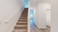 Located at 38389 Honey Suckle Dr in Dade City, Pasco County, Florida, this two-story home presents a clean, modern aesthetic with consistent finishes across both levels. The main floor features wood-look plank flooring that flows through the primary living and kitchen areas, contributing to a bright, cohesive feel. The kitchen is well-appointed with white shaker-style cabinetry, granite countertops with subtle veining, a center island with an undermount sink, and a full suite of stainless steel appliances including a refrigerator, range, microwave, and dishwasher. Recessed lighting illuminates the space efficiently.

A carpeted staircase with a clean white railing leads to the upper level, where wood-look flooring continues in the hallway. The bedrooms are carpeted and generously sized, with one featuring direct access to a private bathroom and a walk-in closet outfitted with wire shelving systems. The bathrooms are finished with wood-look tile flooring, white vanities, and tub-shower combinations with tile surrounds. Throughout the home, white walls, recessed lighting, and consistent trim details create a fresh, move-in-ready environment.