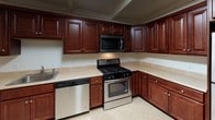 Located at 5055 William Flynn Highway in Gibsonia, PA, this single-floor unit offers a practical and comfortable layout designed for everyday living. The kitchen is a standout feature, showcasing rich cherry wood cabinetry, light countertops, and a full suite of stainless steel appliances including a gas range, over-the-range microwave, and dishwasher. The tile flooring in the kitchen provides a clean, durable surface, while ample cabinet storage ensures excellent organization. The living area is generously sized, featuring soft wall-to-wall carpeting, neutral white walls, and structural beam detailing along the ceiling that adds architectural character. A window allows natural light to filter into the space, creating a bright and open feel. The bedroom includes a full closet with a bi-fold door and built-in hanging rod, offering practical storage. The full bathroom is neatly finished with a wood vanity, granite-style countertop, a large mirror, and a tub-shower combination. A particularly convenient feature is the dedicated in-unit laundry area, which houses a stacked washer and dryer unit. Throughout the space, the consistent use of neutral tones and clean finishes creates a cohesive and move-in-ready environment.