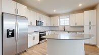 Located on Keymar Drive in Davenport, Florida, this single-story home presents a clean, contemporary design with a neutral color palette carried consistently throughout. The layout, as visible in the 3D floor plan, offers a well-organized arrangement of living, kitchen, bedroom, and bathroom spaces that flow efficiently from one area to the next.

The kitchen serves as a standout feature, showcasing white shaker-style cabinetry with matte black hardware, gray quartz countertops, and a full suite of stainless steel appliances including a refrigerator, range, and over-the-range microwave. A curved kitchen island provides additional prep and seating space, while subway tile backsplash and recessed lighting add a polished finish. A window above the sink allows natural light to brighten the workspace.

Living and secondary areas are finished with light wood-look flooring, while the bedroom features plush neutral carpeting and a bank of windows fitted with white blinds. Ceiling fans are installed throughout, supporting comfort in Florida's climate.

The bathroom is well-appointed with a dual-sink white vanity, gray countertops, matte black fixtures, a large mirror with vanity lighting, and a glass-enclosed shower. The walk-in closet includes wire shelving along two walls. A programmable thermostat supports efficient climate control throughout the home.