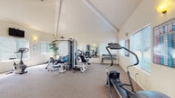Located at 1436 N Cormorant Pl in Boise, Idaho, this single-floor fitness center is thoughtfully designed to support a well-rounded workout experience. The space is defined by its striking vaulted ceilings with exposed beams, which lend an open, airy atmosphere throughout. Neutral-toned carpeting and warm wall sconces complement the light-filled interior, with multiple windows fitted with horizontal blinds allowing generous natural light to pour in from multiple sides.

The facility is well-equipped for both cardio and strength training. Cardio offerings include treadmills, an elliptical trainer, upright and recumbent stationary bikes, and a stair climber. For strength training, a multi-station cable machine, adjustable bench, and a dedicated dumbbell rack with a full set of free weights are available, along with stability balls for functional fitness exercises.

A large wall-mounted mirror expands the sense of space and allows users to monitor their form during workouts. A wall-mounted flat-screen television and an additional monitor are present for entertainment. Practical amenities include a water cooler, a bulletin board, and informational fitness charts posted on the walls. The space offers a clean, well-maintained environment suitable for a comprehensive fitness routine.