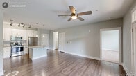 This thoughtfully designed one-bedroom, one-bathroom residence in Apex, NC delivers a comfortable and functional living experience across a single floor. The open-concept kitchen and living area forms the heart of the home, featuring rich hardwood-style flooring, a ceiling fan, and French doors that lead to an outdoor balcony, flooding the space with natural light. The kitchen is a standout, boasting crisp white shaker cabinetry, granite countertops, a subway tile backsplash, stainless steel appliances including a refrigerator, range, microwave, and dishwasher, and a central island with pendant lighting — ideal for both cooking and entertaining. The spacious bedroom is finished with plush wall-to-wall carpeting, a ceiling fan with light fixture, and a window offering pleasant outdoor views. The full bathroom impresses with a double-sink vanity topped with granite counters, white cabinetry, tile flooring, and a tiled walk-in shower. A dedicated closet provides ample storage, while the in-unit laundry area accommodates a full-size side-by-side washer and dryer. Neutral gray tones and white trim throughout lend the space a clean, modern aesthetic.