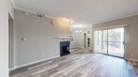 This well-appointed single-floor residence offers a clean, modern aesthetic carried consistently throughout every room. The open living area serves as the heart of the home, anchored by a sleek fireplace with a dark surround and white mantle, complemented by crown molding and track lighting overhead. Wood-look luxury vinyl flooring runs seamlessly throughout the entire space, lending warmth and visual continuity. A large sliding glass door floods the living area with natural light and provides direct access to an outdoor balcony or patio, while vertical blinds offer privacy and light control.

Adjacent to the living room, a pass-through with a mirrored accent wall connects to the kitchen, which is thoughtfully designed with white shaker-style cabinetry, quartz countertops, a mosaic tile backsplash, and a full suite of stainless steel appliances including a range, microwave, dishwasher, and refrigerator. A window above the sink brings in additional natural light.

The bedroom is a comfortable, well-lit retreat featuring a ceiling fan, a sliding glass door, and a closet. The bathroom is finished with quartz countertops, wood-toned cabinetry, and a full tub-and-shower combination with white tile surround. Throughout the space, neutral tones create a calm and cohesive atmosphere.