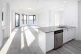 Located at 30 Hanmer Street in Barrie, Ontario, this modern unit offers a bright, open-concept layout finished in a clean, contemporary palette throughout. Light-toned engineered hardwood flooring flows seamlessly across the entire space, complementing the crisp white walls and ceilings.

The living area is a standout, bathed in abundant natural light courtesy of large, black-framed windows that wrap around a curved corner, offering expansive elevated views of the surrounding Barrie cityscape. The open-concept kitchen features a generous island with a quartz-style countertop and integrated sink, white cabinetry, and a full suite of stainless steel appliances including a refrigerator, stove, microwave, and dishwasher.

The bedroom is well-proportioned and includes a mirrored sliding closet as well as access to a dedicated walk-in closet with wire shelving and hanging rods. Large windows in the bedroom frame wide outdoor views, maintaining the airy feel found throughout the unit. The bathroom is finished with a white vanity, neutral countertop, a combined tub and shower enclosure, and a well-lit mirror. The unit is accessed through a solid entry door, completing this thoughtfully designed, move-in ready space.