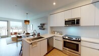 Located on West Pico Boulevard in Los Angeles, this modern single-floor residence offers a thoughtfully designed open-concept layout with clean lines and contemporary finishes throughout. The kitchen is a standout feature, showcasing sleek white flat-front cabinetry extending to the ceiling, a suite of stainless steel appliances including a French door refrigerator, electric range, built-in microwave, and dishwasher, all centered around a peninsula with a deep stainless steel sink and white quartz countertops. Warm wood-look flooring flows seamlessly through the living and dining areas, where a round dining table sits beneath a textured pendant light, complemented by open shelving and a textured accent wall that adds warmth and depth. The bedroom is a serene retreat, featuring large windows that frame sweeping city views, a textured wallcovering accent wall, and an abundance of natural light. The bathroom is elegantly appointed with a floating white vanity, expansive mirror, and a walk-in closet, all finished with neutral tile flooring. Throughout the space, the interplay of natural textures, modern fixtures, and carefully curated design elements creates a cohesive, inviting atmosphere ideal for contemporary urban living.
