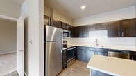 This single-story unit offers a thoughtfully designed layout that maximizes functionality across its one bedroom and one bathroom. The kitchen serves as a standout feature, showcasing dark espresso-toned shaker cabinets extending to the ceiling for abundant storage, complemented by light quartz countertops, a white hexagonal tile backsplash, and a full suite of stainless steel appliances including a refrigerator, electric range, built-in microwave, and dishwasher. A peninsula counter provides additional workspace and casual seating. Light wood-style flooring runs throughout the main living area, lending warmth and continuity to the space.

The generously sized primary bedroom is finished with plush carpeting, neutral-toned walls, a ceiling fan, and a window that admits natural light. A dedicated closet with built-in shelving offers organized storage. The bathroom features a full soaking tub and shower combination enclosed by classic white subway-style tiling with a contrasting gray accent band, providing a clean and timeless aesthetic throughout.
