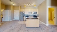 Located at 4437 Glengarry Dr in Beavercreek, Ohio, this single-floor residence offers a thoughtfully designed layout with a cohesive neutral palette throughout. The kitchen is a functional centerpiece, equipped with stainless steel appliances including a refrigerator, range, microwave, and dishwasher. Light wood cabinetry provides ample storage, while dark granite countertops add contrast. A central island with a matching granite surface and pendant lighting overhead enhances both workspace and style. Track lighting above the kitchen adds further illumination. The kitchen flows seamlessly into the open living area, which features plush carpeting, warm beige walls, and large windows that invite abundant natural light. One room opens directly onto a balcony through glass French doors topped with a transom window, offering outdoor access and additional brightness. A second carpeted bedroom features a generously sized window with exterior views. The bathrooms are finished with light tile flooring, wood-toned vanity cabinetry, and white tub-shower combinations with chrome fixtures. The overall ambiance is clean, modern, and move-in ready, with consistent finishes and a practical open-concept design that maximizes the use of space throughout.