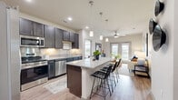 Located in San Marcos, TX, this well-appointed 2-bedroom, 2-bathroom residence offers a thoughtfully designed single-level layout. The open-concept kitchen is a standout feature, showcasing rich dark cabinetry, granite countertops, stainless steel appliances including a side-by-side refrigerator, built-in microwave, and range, as well as a central island with bar seating and pendant lighting — ideal for both cooking and casual dining. Wood-style flooring flows throughout, adding warmth and continuity to the space. The living room is bright and welcoming, highlighted by a ceiling fan, neutral walls, and French doors that open to an outdoor view of the surrounding greenery. The primary bedroom is generously sized, featuring large windows that bring in abundant natural light and offer pleasant outdoor views. Both bathrooms are finished with granite-topped dark vanities, full-width mirrors, and wood-style flooring. The primary bath includes a walk-in closet with built-in wire shelving and a soaking tub, providing a functional and comfortable retreat. The second bathroom mirrors the same refined finishes. A dedicated walk-in closet with multi-tier wire shelving adds practical storage. The overall aesthetic is clean, modern, and cohesive throughout.
