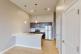 Located at 4005 State Farm Pkwy in Columbia, MO, this well-designed one-bedroom, one-bathroom unit offers a thoughtful, efficient layout across a single floor. The open-concept kitchen and living area serves as the heart of the home, featuring striking dark espresso cabinetry that reaches toward the soaring ceilings, crisp white quartz countertops, and a full suite of stainless steel appliances including a refrigerator, electric range, and built-in microwave. A large peninsula island with an undermount sink and stylish pendant lighting above adds both functionality and visual appeal. Light-toned hardwood-style flooring runs throughout, tying the space together with a warm, contemporary feel. The bedroom is comfortably sized, offering a window with natural light and access to two closets, providing ample storage. The bathroom is clean and modern, outfitted with a tub-shower combination, a dark-cabinetry vanity with a white countertop, and matching flooring. Additional practical spaces include a dedicated laundry area, utility room, pantry, and entrance foyer. A private balcony with metal railing offers outdoor access and open views of the surrounding area.