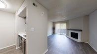 Located at 4031 Thousand Oaks Dr in San Antonio, Texas, this single-floor unit offers a well-organized layout with a clean, neutral aesthetic throughout. The living room serves as the heart of the space, showcasing wood-style flooring, a textured ceiling, and a classic tile-surround fireplace with a sleek mantle. A large sliding glass door dressed with vertical blinds fills the room with natural light and provides access to the outdoors. The open-concept design connects the living area to the kitchen, which features dark cabinetry, a black electric range, a stainless steel sink, and stone-look countertops, along with a pass-through bar that enhances the flow between spaces. A separate dining or flex area is accessible directly from the kitchen. The bedroom is a comfortable, well-lit retreat with a ceiling fan, a window with blinds, and wood-style flooring. A generously sized walk-in closet with dual shelving rods and ample storage space serves the bedroom. The bathroom is appointed with a dark-framed vanity mirror, stone-look countertop, and a full tub-shower combination. Consistent flooring and a neutral color palette tie the entire unit together, creating a cohesive and inviting atmosphere.