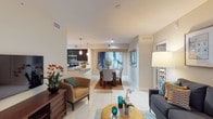 This single-floor residence offers a thoughtfully designed open-concept layout connecting the living, dining, and kitchen areas. The living room features light tile flooring, a sliding glass door opening to a private patio with views of mature tropical landscaping, and contemporary décor accented by a gallery wall arrangement. The kitchen is outfitted with dark espresso cabinetry, stainless steel appliances, a tile backsplash, and an expansive granite-topped breakfast bar with pendant lighting overhead, flowing seamlessly into a dedicated dining area.

The residence includes multiple bedrooms, each featuring wood-look flooring, natural light from windows dressed with blinds and patterned draping, and ample space for furnishings. Two bathrooms serve the home: one with a glass-enclosed walk-in shower, dark vanity cabinetry, and granite countertops; the other featuring a soaking tub with shower combination, granite countertops, and bold accent wall coloring. Throughout, neutral warm tones and consistent finishes create a cohesive, modern ambiance suited for comfortable everyday living.