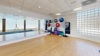 Located at 4129 Hearthside Dr in Wilmington, NC, this fitness center offers a thoughtfully designed, single-floor layout that provides ample space for a full range of exercise activities. The facility is divided into two distinct areas, each serving a specific fitness purpose.

The main gym area features durable rubber flooring and is outfitted with an extensive selection of equipment, including treadmills, elliptical trainers, recumbent bikes, stair climbers, cable machines, weight benches, and a full dumbbell rack. Floor-to-ceiling mirrors line portions of the walls, enhancing the sense of space and allowing for form checks during workouts. Motivational wall graphics add an energizing atmosphere throughout. Overhead, a drop-tile ceiling with recessed panel lighting ensures bright, even illumination across the entire workout floor.

The second area is a dedicated group exercise and yoga studio featuring warm hardwood flooring and a striking curved wall of glass block that allows soft, diffused natural light to fill the room. Full-length mirrors, foam exercise mats, stability balls, resistance equipment, and step platforms are neatly stored along the walls, making the studio versatile for yoga, stretching, dance, or group fitness classes. Together, the two areas create a comprehensive and welcoming fitness facility suited for a wide variety of training needs.