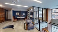Located at 401 W Hargett St in the heart of downtown Raleigh, NC, this thoughtfully designed single-floor commercial space blends contemporary style with warm, character-rich materials. The layout offers a variety of seating configurations to support both focused work and collaborative gatherings, including cushioned lounge chairs, round tables with modern chairs, and high bar-top seating along a wall-mounted counter beneath a large, vibrant piece of artwork.

A standout feature is the glass-enclosed conference or meeting room, framed in sleek dark metal and offering clear sightlines while maintaining acoustic separation. Large windows throughout the space invite abundant natural light and provide views of the surrounding urban streetscape, keeping the interior feeling open and connected to the city outside.

The design palette combines deep navy blue accent walls, exposed brick, and neutral carpeted flooring with a subtle linear pattern, creating a professional yet approachable atmosphere. A dramatic reclaimed wood accent wall near the stairwell adds warmth and texture, serving as a compelling architectural focal point that nods to the building's historic character.

Linear LED lighting runs across the ceilings, providing consistent, well-distributed illumination throughout. The overall ambiance is polished and purposeful, ideal for productivity and professional interaction in a dynamic urban setting.