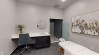 Haven on Tucker is a thoughtfully designed single-floor wellness suite built to provide a calm, professional environment for therapeutic services. The treatment room serves as the centerpiece of the space, featuring large-format dark gray tile flooring that extends throughout and contributes to a clean, grounded aesthetic. Neutral light gray walls keep the atmosphere serene and uncluttered, while black-trimmed doors add a sharp, contemporary contrast.

A professional massage table positioned at the heart of the room establishes the space's primary function, offering ample circulation area around it. A built-in dark cabinetry vanity with a white countertop and round gold-framed mirror provides a practical and stylish workstation, complemented by a teal ergonomic chair. Curated wall art adds a refined artistic touch without overwhelming the minimalist design.

Adjacent to the main treatment area, a walk-in shower enclosure features floor-to-ceiling dark subway tile walls and a natural pebble stone floor, delivering a spa-like experience. A frosted glass panel offers a tasteful division between the treatment and shower areas. The overall design of Haven on Tucker balances functional professionalism with elevated wellness aesthetics, making it well-suited for massage therapy, bodywork, or other personal care services.
