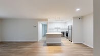 Located at 5029 Columbia Rd in Columbia, MD, this single-floor, 2-bedroom, 2-bathroom residence offers a clean, modern aesthetic throughout. The open-concept living and kitchen area serves as the heart of the home, where light wood-tone luxury vinyl flooring extends underfoot and a sliding glass door fills the living room with natural light while providing access to the outdoors. The kitchen is outfitted with crisp white shaker-style cabinetry, stainless steel appliances including a refrigerator, dishwasher, and range, a subway tile backsplash, and a peninsula that adds both counter space and a casual dining option. Track and skylight-style ceiling fixtures keep the kitchen well-lit throughout the day. Both bedrooms feature plush wall-to-wall carpeting and neutral tones, with the primary bedroom distinguished by a large bay window arrangement that invites ample natural greenery views. A dedicated closet adds practical storage. The two bathrooms are finished in a clean, contemporary style with white vanities, light countertops, and wood-tone flooring. One bathroom includes a full tub-shower combination with a gold-toned curtain rod accent. The overall palette of soft whites and warm neutrals creates a cohesive, move-in ready atmosphere throughout the home.