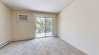 Located at 1860 52nd St E in Inver Grove Heights, MN, this two-bedroom, one-bathroom unit offers a practical and comfortable single-floor layout. The living room is generously sized, featuring wall-to-wall carpet, a sliding glass door that opens to a balcony with tree-lined views, and a wall-mounted air conditioning unit alongside baseboard heating. The open connection to the kitchen creates an easy flow between living and dining areas. The galley-style kitchen is well-appointed with ample upper and lower cabinetry in a light wood and white finish, a white appliance suite including a refrigerator, electric range, and over-the-range microwave, and durable tile flooring beneath a bright skylight and ceiling fan. Both bedrooms are carpeted and include baseboard heating; the primary bedroom features a mirrored sliding closet and access to a walk-in closet with built-in shelving rods. A second carpeted bedroom offers a ceiling fan and a large window with leafy outdoor views. The full bathroom includes tile flooring, a vanity with storage, and a tub/shower combination. A hallway connects all rooms, completing this well-organized and functional floor plan.