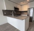 This 410 sq ft one-bedroom apartment at 14529 104A Ave in Surrey, BC, offers a well-designed modern living space across a single floor. The open-concept kitchen and living area is anchored by a contemporary kitchen featuring white flat-panel cabinetry extending to the ceiling, a quartz countertop peninsula with an undermount sink, tile backsplash, stainless steel appliances including a refrigerator and over-the-range microwave, and track lighting overhead. Consistent wood-look laminate flooring runs throughout the entire unit, lending warmth and visual continuity. The living area benefits from large sliding glass doors that open to an outdoor space, allowing abundant natural light and exterior views of the surrounding neighbourhood. A wall-mounted ductless mini-split air conditioning unit and baseboard heaters ensure year-round comfort. The 120 sq ft bedroom is a bright, clean space featuring a large window with outdoor views, a double sliding-door closet, and continued laminate flooring. Clean white walls, modern white interior doors, and a neutral colour palette throughout give the unit a fresh, move-in-ready aesthetic. The entry foyer provides a functional transition into the living space, completing this efficiently designed urban apartment.