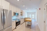 This well-appointed one-bedroom, one-bathroom residence in Waltham, MA offers a thoughtfully designed single-floor layout with a bright, modern aesthetic throughout. Light hardwood-style flooring flows through the main living areas, complementing the clean white walls and recessed lighting that keep the space feeling open and airy.

The kitchen is a standout feature, showcasing light wood cabinetry, granite countertops, a white subway tile backsplash, and a full suite of stainless steel appliances including a French door refrigerator, electric range, microwave, and dishwasher. The kitchen opens seamlessly into the combined dining and living area, which is anchored by a set of glass French doors that invite natural light and outdoor views of the community courtyard and pool area.

The bedroom offers plush carpeting, a large window with courtyard views, and direct access to a well-organized walk-in closet with built-in shelving, hanging rods, and drawer units. The full bathroom impresses with a frameless glass walk-in shower with tile surround, a granite-topped double vanity with light wood cabinetry, and hardwood-style flooring. Additional conveniences include a dedicated laundry area and utility room, rounding out this efficient and stylish Waltham residence.