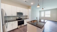 This single-floor residence in Jacksonville, FL (32207) offers a clean, contemporary design with consistent dark hardwood-style flooring flowing throughout the entire unit. The open-concept layout seamlessly connects the kitchen and living areas, creating a spacious, functional environment.

The kitchen serves as the centerpiece of the unit, anchored by a large island with dark granite countertops and a double stainless steel undermount sink. Sleek white cabinetry extends to the ceiling, paired with a neutral gray subway tile backsplash. Stainless steel appliances, including a range, built-in microwave, and refrigerator, complete the modern aesthetic. Stylish industrial-inspired pendant lights hang above the island, adding a distinctive design touch.

The living area benefits from natural light through large windows and French doors, the latter also providing outdoor access and featuring a ceiling fan overhead. Neutral-toned walls create a versatile backdrop throughout the space.

The bathroom is well-appointed with granite countertops, white cabinetry, a large vanity mirror, and a full tiled tub-shower combination. Additional rooms include a generously sized bedroom with dual windows and a walk-in closet, further enhancing the unit's practical appeal.