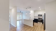 Located at 1215 Evolve Way in Greenville, NC, this one-bedroom, one-bathroom unit offers a well-designed single-floor layout that maximizes functionality and comfort. The open-concept living, dining, and kitchen area serves as the heart of the home, unified by warm light wood-style flooring and recessed lighting throughout. The kitchen is a standout feature, boasting two-tone cabinetry with crisp white upper cabinets and dark lower cabinets, a geometric tile backsplash, granite countertops, and a full suite of stainless steel appliances including a refrigerator, range, and microwave. A central island with a built-in sink and pendant lighting above adds both style and utility. The living area is bright and airy, enhanced by a ceiling fan and access to a private patio through glass-panel doors. The bedroom is carpeted for comfort, fitted with a ceiling fan, and features a window with outdoor views. The bathroom mirrors the kitchen's refined aesthetic, offering granite countertops, white cabinetry, and a glass-enclosed shower. Additional conveniences include an in-unit laundry room with a full-size washer and dryer, a pantry, two closets, and a dedicated utility room, rounding out this efficiently planned home.