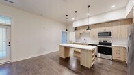Located at 550 Great Circle Rd in Nashville, TN, this thoughtfully designed two-bedroom, one-bathroom residence offers a contemporary living experience on a single floor. The open-concept kitchen, dining, and living area serves as the heart of the home, featuring light wood cabinetry extending to the ceiling, white quartz countertops, a subway tile backsplash, stainless steel appliances including a French door refrigerator and gas range, and a freestanding island with pendant lighting overhead. Rich hardwood-style flooring flows seamlessly throughout the entire space, complementing the clean, neutral palette. The primary bedroom is generously sized and includes a ceiling fan, direct access to a private balcony with outdoor views, and a spacious walk-in closet with built-in wire shelving. The second bedroom features tall ceilings and a built-in shelved closet for ample storage. The bathroom is finished with a light wood vanity, white countertop, and a glass-enclosed walk-in shower with classic subway tile. Additional conveniences include a dedicated laundry area, pantry, utility room, and three closets total. The overall ambiance is bright, clean, and modern, offering a well-organized and functional layout ideal for comfortable everyday living.