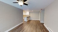 This single-floor, 2-bedroom, 1-bathroom residence offers a thoughtfully designed open-concept layout that maximizes functionality and comfort. The main living area is finished with warm wood-look luxury vinyl plank flooring that flows throughout, complemented by crisp white baseboards and neutral gray walls that create a clean, contemporary aesthetic.

A ceiling fan with a light fixture is centrally positioned in the living area, ensuring year-round comfort and ample illumination. Recessed lighting adds a modern touch to the ceiling, brightening the space naturally and evenly.

The kitchen is seamlessly integrated into the living area and features white cabinetry, a breakfast bar peninsula that serves as a natural divider between the kitchen and living space, and light-toned countertops. This open connection between the kitchen and living room makes the space ideal for both daily living and casual entertaining.

The overall color palette — soft grays, white trim, and natural wood tones — lends the unit a fresh, move-in-ready feel. The layout is efficiently organized, with clearly defined zones for living, dining, and cooking, all contained within a compact yet comfortable footprint. The clean finishes and modern details throughout reflect a well-maintained, updated interior.