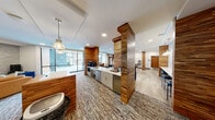 Located at 1819 N Meridian St in Indianapolis, this well-appointed single-floor amenity space offers a thoughtfully designed layout that seamlessly blends social and recreational areas. Distinctive wood-clad columns punctuate the open floor plan, adding warmth and architectural character throughout.

The kitchen and dining area serve as a central hub, featuring a sleek white quartz island with bar seating, stainless steel appliances, and pendant lighting. Adjacent dining space includes a round wood table surrounded by plush purple velvet chairs, complemented by woven pendant fixtures, floating wood shelves, and a modern fireplace wall feature.

The living room lounge is anchored by a striking stacked-stone accent wall with a wall-mounted TV and a floating wood ledge. Blue velvet chairs and a tan leather sofa create an inviting seating arrangement, while floor-to-ceiling windows flood the space with natural light and offer outdoor views.

The game room showcases a full-size pool table set against light hardwood flooring, with a stone-accented bar counter, black barstools, and additional lounge seating. A separate dining nook near large windows overlooks an outdoor courtyard, providing a bright and casual gathering spot. The cohesive design, blending natural textures with contemporary furnishings, creates an engaging and versatile communal environment.