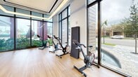Located at 501 NW Seventh Ave in Fort Lauderdale, FL, this contemporary fitness center delivers a comprehensive, high-design workout environment across a single, expansive floor. The space is defined by its bold aesthetic, featuring striking red perforated ceiling panels with integrated linear lighting that run the length of the main exercise floor, set against dark charcoal walls and durable light-toned flooring. Floor-to-ceiling windows line the perimeter, flooding the interior with natural light and offering open views of the surrounding greenery and streetscape. The main workout hall is generously proportioned, accommodating a full suite of cardio equipment — including treadmills, stair climbers, ellipticals, and stationary bikes — as well as a dedicated strength training zone with cable machines, weight benches, and a free weights rack. A separate spin studio features hardwood flooring, floor-to-ceiling mirrors framed in teal, built-in storage cubbies, and its own set of cycling bikes. An additional mirrored training room with teal accent walls and hardwood floors provides space for functional training, with kettlebells, medicine balls, and resistance equipment readily available. A welcoming lounge area near the entrance features bold red modern seating and large-scale abstract mural art. Two bathrooms and a closet round out the facility's amenities.