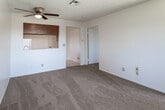 Located at 250 Wilkerson Ave in Perris, California, this single-story unit offers a straightforward and functional layout designed for comfortable everyday living. The living area is generously sized, featuring warm neutral carpeting, a textured ceiling, and a ceiling fan with light fixture that provides both airflow and ambient lighting. A distinctive pass-through window with a wood-trimmed header connects the living space to the kitchen, creating an open feel between the two areas. The kitchen is equipped with warm wood cabinetry, white appliances including a gas range and refrigerator, a corner sink, and tile flooring that adds easy-care practicality. Natural light filters in through a window fitted with vertical blinds. The bedrooms are well-proportioned, each featuring plush carpeting, textured ceilings, and windows with vertical blinds that allow for natural light and outdoor views of the surrounding greenery. Ceiling fans are present in select rooms for added comfort. The bathroom includes a full tub and shower combination, tile flooring in a neutral tone, and a clean, functional design. Throughout the unit, the consistent use of neutral tones and carpet creates a cohesive and move-in ready environment.
