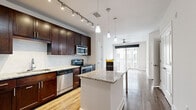 Located in the heart of downtown Orlando at 480 N Orange Ave, this well-appointed one-bedroom, one-bathroom unit offers a thoughtfully designed single-floor layout. The open-concept kitchen is a standout feature, showcasing rich dark-espresso cabinetry reaching to the ceiling, granite countertops, a full suite of stainless steel appliances including a refrigerator, electric range, microwave, and dishwasher, and a central island with pendant lighting overhead. Track lighting and light wood-style flooring complete the kitchen's polished look, flowing seamlessly into the living area. The living room is bright and airy, benefiting from large sliding glass doors that open to a private balcony, while a ceiling fan adds comfort. The bedroom features soft carpeting, a ceiling fan, a dedicated closet, and a window that brings in natural light. The bathroom is finished with granite-topped vanity cabinetry, large-format tile flooring, and a tiled tub/shower combination. Clean white walls and crisp trim throughout the unit create a bright, neutral aesthetic. A hallway and entrance area complete the efficient and functional floor plan.