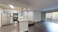 This single-floor residence offers a thoughtfully designed open-concept layout that connects the kitchen, dining, and living areas into one cohesive space. The kitchen is well-equipped with stainless steel appliances, including a refrigerator, electric range, and over-the-range microwave. Gray shaker-style cabinetry pairs with light granite countertops and a subtle tile backsplash, while a peninsula with a built-in sink provides additional prep space and separates the kitchen from the main living area. Dark hardwood-style flooring runs throughout the common areas, adding warmth and continuity to the space.

The living area is generously sized and features neutral gray walls, recessed lighting, and a raised platform section that adds architectural interest. A sliding glass door provides access to an outdoor area and brings in natural light. A hallway leads to the private quarters, where bedrooms feature plush carpeting, ceiling fans with light fixtures, and windows that allow natural light to filter in.

The bathroom features a granite-topped vanity with gray cabinetry, brushed nickel hardware, and a tub-shower combination with clean white tile surround. Throughout the residence, the neutral color palette and modern finishes create a clean, contemporary ambiance.
