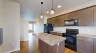 This two-floor residence offers a thoughtfully designed layout with modern finishes throughout. The main living area welcomes occupants with warm hardwood-style flooring, neutral-toned walls, and a wall sconce that adds ambient lighting near the front entry door.

The kitchen is a standout space, featuring rich dark-brown shaker-style cabinetry extending to the ceiling for ample storage. Granite-look countertops line the perimeter and a central island, while black stainless appliances—including a refrigerator, electric range, and over-the-range microwave—provide a cohesive aesthetic. Pendant lighting with glass shades hangs above the island, enhancing both function and style.

Bedrooms are carpeted for comfort and receive natural light through multiple windows. The primary bedroom includes dual closets with rod systems, offering generous storage. The bathroom features wood-toned cabinetry, white countertops, hardwood-style flooring, and a tub-shower combination.

A notable highlight is the expansive rooftop terrace on the second floor, finished with brick pavers and framed by a metal railing and privacy panel, offering open views of surrounding greenery.