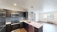 Located in the Roxborough neighborhood of Philadelphia, this thoughtfully designed one-bedroom, one-bathroom unit offers a modern living experience with high-quality finishes throughout. The open-concept kitchen and living area serves as the heart of the home, featuring dark matte cabinetry, stainless steel appliances including a refrigerator, range, and over-the-range microwave, as well as a sleek white quartz peninsula with an undermount sink and pendant lighting overhead. A blue-gray subway tile backsplash adds a stylish accent, complementing the contemporary color palette. Warm hardwood-style flooring flows throughout the main living spaces, enhancing the cohesive and modern aesthetic. Recessed lighting keeps the open area bright and inviting. The bedroom is a well-proportioned retreat featuring a window with natural light, a wall-mounted HVAC unit, and the same hardwood-style flooring. A dedicated closet provides practical storage. The bathroom is cleanly appointed with large-format gray tile flooring, a dark navy vanity with brass hardware, a white quartz countertop, a mirror, and warm vanity lighting above. The space combines functional design with contemporary style, making it an efficient and attractive urban residence.