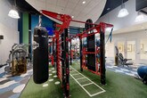 Located at 5405 Tuckerman Ln in North Bethesda, MD, this expansive fitness center delivers a well-appointed and energetic workout environment spread across a single, generously sized floor. The space is defined by striking interior design, including a bold scallop-patterned carpet in blue, grey, and white tones that adds visual dynamism throughout the cardio and strength training areas. Vibrant accent walls in deep green and teal punctuate the white walls, contributing to an energizing atmosphere.

The cardio zone is equipped with multiple modern treadmills featuring integrated digital screens, elliptical machines, stair climbers, and stationary bikes — all oriented toward wall-mounted televisions for an engaging workout experience. Pendant lighting fixtures hang from the ceiling, complementing the recessed lighting and creating a well-lit environment throughout.

A dedicated functional training area features artificial turf laid out with field markings, lined with a red multi-purpose rack system stocked with medicine balls, battle ropes, and resistance equipment. Strength training machines are thoughtfully arranged across the main floor, offering a comprehensive range of options. A dramatic open staircase with black metal railings adds architectural interest and visual height to the space, enhancing the sense of openness. Large mirrors along the walls further amplify the spacious feel of this fully equipped fitness facility.