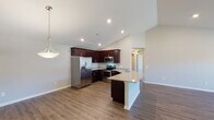 This two-story home is designed with a thoughtful open-concept layout on the main level, where vaulted ceilings lend a sense of spaciousness to the living and kitchen areas. The kitchen is a standout feature, showcasing rich dark-mahogany cabinetry that extends to the ceiling, granite countertops with speckled light tones, and a full suite of stainless steel appliances including a French door refrigerator, electric range, and built-in microwave. A peninsula with an integrated sink provides additional workspace and a natural division between the kitchen and the expansive living area. Durable wood-look flooring flows throughout the main level, complementing the neutral, light-toned walls. A half bathroom on this floor features matching granite countertops and dark cabinetry. The attached garage offers generous space with a concrete floor and automatic opener. Upstairs, carpeted bedrooms provide a comfortable retreat, with windows allowing natural light and outdoor views. A full bathroom on the upper level includes a walk-in glass shower, granite vanity countertop, dark cabinetry, and tile flooring, maintaining the consistent design language found throughout the home.
