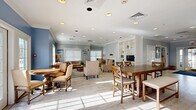 Located at 502 W River Rd in Hooksett, New Hampshire, this thoughtfully designed single-floor space offers a warm, coastal-inspired atmosphere across a comfortable footprint. Light hardwood-style flooring, crisp white crown molding, and a soft palette of pale blue and grey tones create a cohesive and inviting ambiance throughout.

The living room serves as a central gathering area, featuring a classic white-mantled fireplace flanked by built-in bookshelves, elegantly appointed seating, and large windows that bathe the room in natural light. Coastal artwork and tasteful furnishings contribute to the relaxed, refined character of the space.

The dining room accommodates both casual and group seating, with a substantial farmhouse-style dining table and cross-back chairs as its centerpiece. French doors open to an outdoor area, enhancing the sense of openness and allowing additional natural light to flow in freely.

The kitchen is fully equipped with stainless steel appliances, including a French door refrigerator, range, microwave, and dishwasher, all complemented by white cabinetry and clean countertops. A breakfast bar with counter-height seating provides an additional dining option adjacent to the kitchen.

Recessed lighting throughout ensures each area is well-lit, and the open layout between rooms promotes a seamless flow ideal for both everyday use and social gatherings.