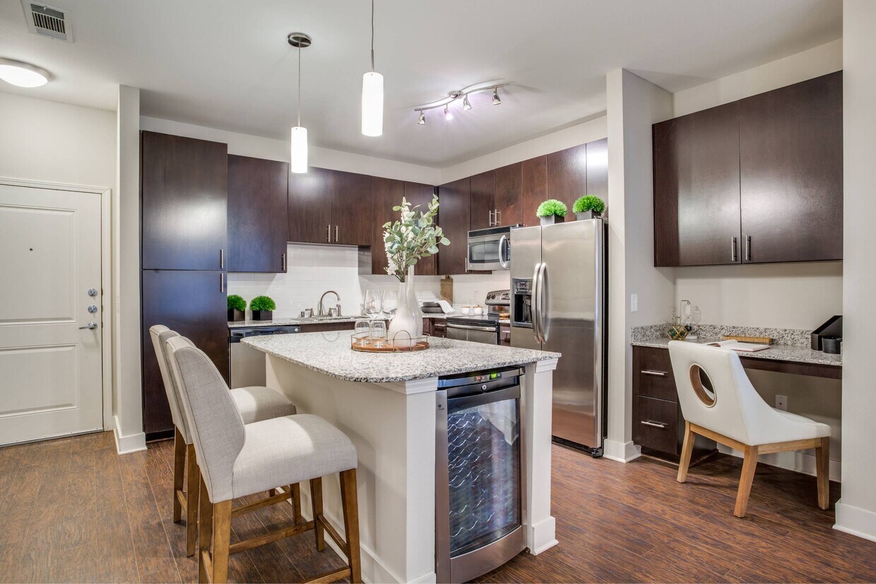 Cocina con isla, encimeras de granito, gabinetes de madera oscura y electrodomésticos de acero inoxidable. - Park Central at Flower Mound