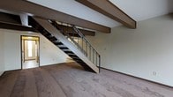 Located at 6175 Northgate Rd in Columbus, Ohio, this two-story residence offers a functional and characterful layout spread across two levels. The main living area immediately draws the eye upward to distinctive exposed wood ceiling beams, which lend a warm, structural charm to the space. Neutral-toned carpeting runs throughout the lower level, contributing to a comfortable and understated ambiance. A prominent open-riser staircase with sleek black metal railings serves as a central architectural feature, connecting the two floors while maintaining an open, airy feel within the main living area. The staircase design allows light to pass through, enhancing the sense of openness. The lower level offers generous open space, ideal for flexible living arrangements. The overall color palette is neutral and clean, with light-toned walls that complement the warm wood tones of the exposed beams above. The two-floor layout provides a natural separation between living and private spaces, making this a well-structured and versatile property in the northside Columbus area.