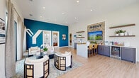 Located in Melissa, Texas, the Yardly Stoneridge sales office is a thoughtfully designed, single-floor welcome center that makes an immediate impression with its vibrant, brand-forward aesthetic. The open-plan interior is anchored by a bold teal accent wall prominently featuring the Yardly "Y" logo, which creates a striking focal point against the crisp white walls and light hardwood flooring that runs throughout the space.

The main area is divided into two functional zones that flow seamlessly into one another. A comfortable lounge area near the entrance offers stylish rounded armchairs and a geometric coffee table arranged atop a soft area rug, providing a welcoming setting for visitors. Adjacent to this is a consultation and reception counter finished in white and navy, complete with bar-height seating and a mounted display screen showcasing community information.

A dedicated resource station along the back wall features floating wood shelves, a gray cabinetry unit, and brochure displays, complemented by the "Find Your Home" branding. Two private rooms with frosted glass doors are accessible from the main floor, ideal for one-on-one consultations.

Large floor-to-ceiling windows and sliding glass doors flood the interior with natural light while offering direct views of the surrounding community and outdoor pool area. The entrance features a full-glass double-door façade, reinforcing the bright and open ambiance of this polished, professionally curated sales environment.